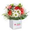 The essence of celebration and joyful giving flourishes in this lush bouquet, beautifully encased within a clean, square white gift bag ready for delivery across all of Sipson. The star blooms-coral and peach-hued carnations-form playful clouds of frilled petals, their cheerful colour impossible to ignore. Dancing between them are crisp white daisies, each bright with a yellow-green center that radiates positivity, much like the lively spirit of local gardens near Sipson Lane. Wispy sprays of baby's breath contribute an airy softness, dazzling the eye with their cloud-like lightness and creating a textured ballet amidst the more structured flowers. A few closed buds, their tips brushed with purple, rest quietly along one side, hinting at tomorrow's blossoms and the continued stories of each bouquet given. All is enveloped in a cascade of shiny, deep green leaves, which gently cradle the flowers, offering a luxuriant contrast. The carefully rounded composition shines beneath soft light, drawing out the radiant freshness and inviting moods of affection and gratitude. This arrangement-crafted with authentic Sipson expertise-captures the joy of thoughtful floristry, whether given as a birthday surprise, anniversary gesture, or simply to lift a neighbour's spirits. The image tells of community connection and artful care, reflecting the very heart of flower gifting in Sipson.